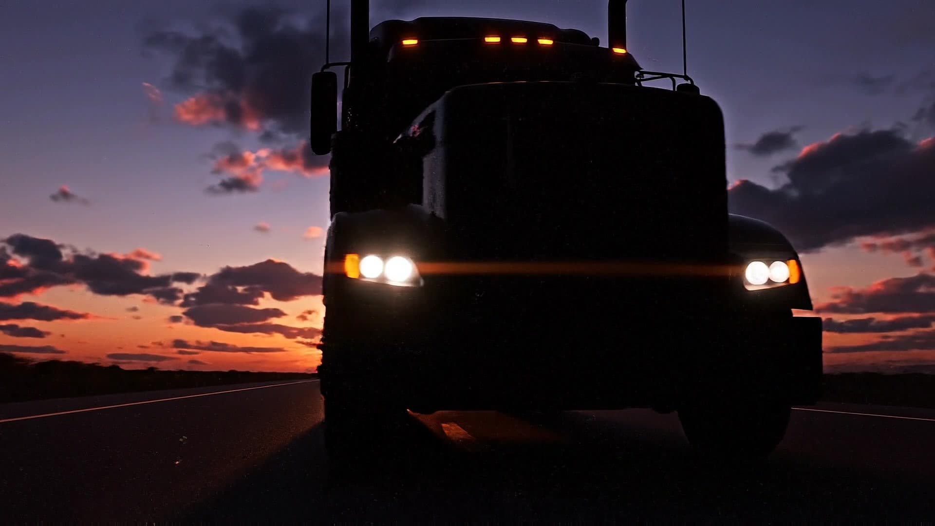 Semi truck rolling toward the sunset on an open highway